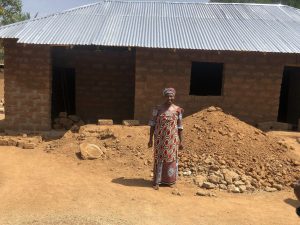 Woman standing in front of re-roofed house in Kaduna State